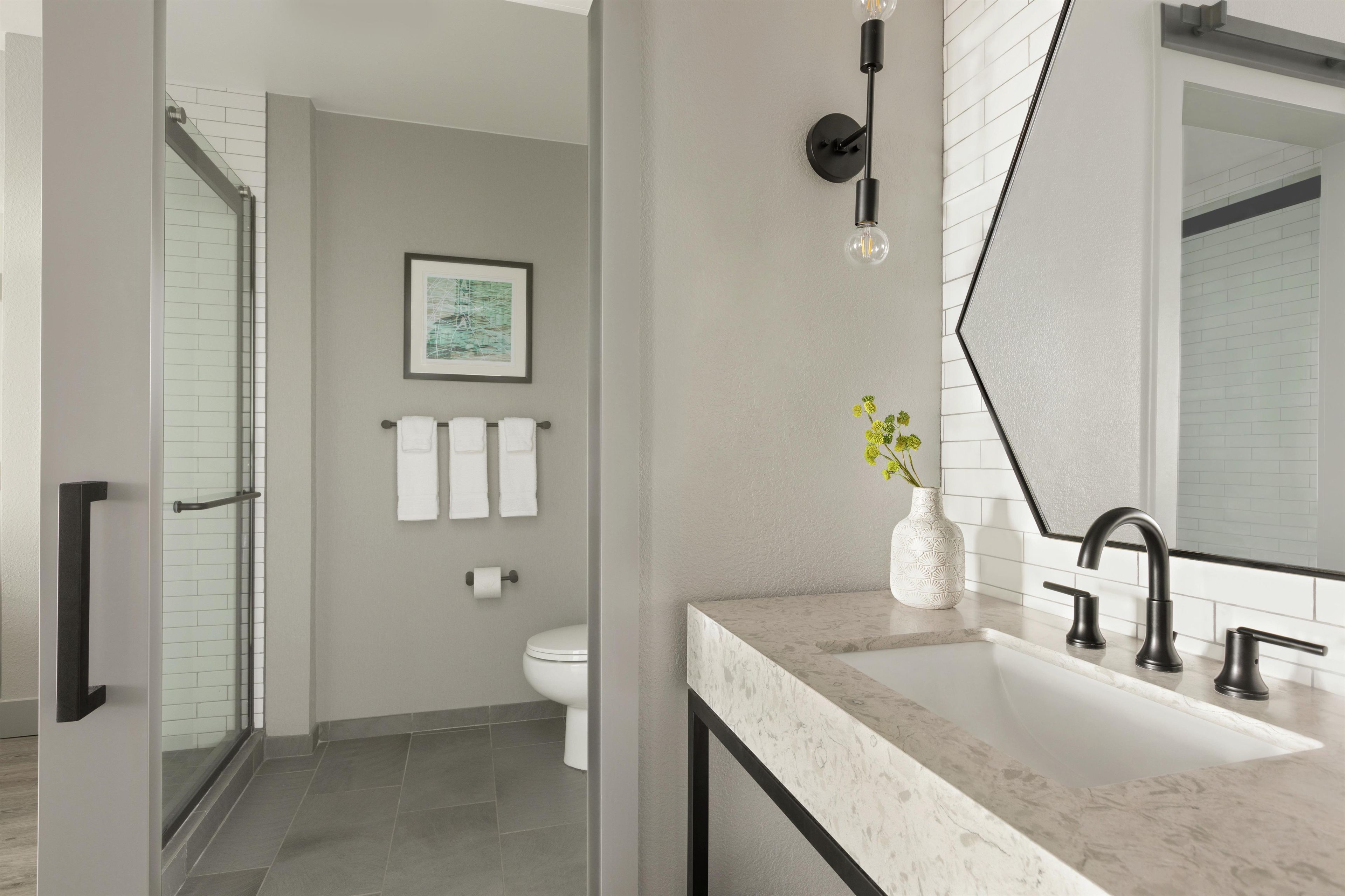 A modern bathroom with a glass shower enclosure, a marble sink, and a large mirror.