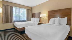 Habitación de hotel con dos camas, un ventanal con cortinas, una lámpara de noche y una alfombra a rayas.