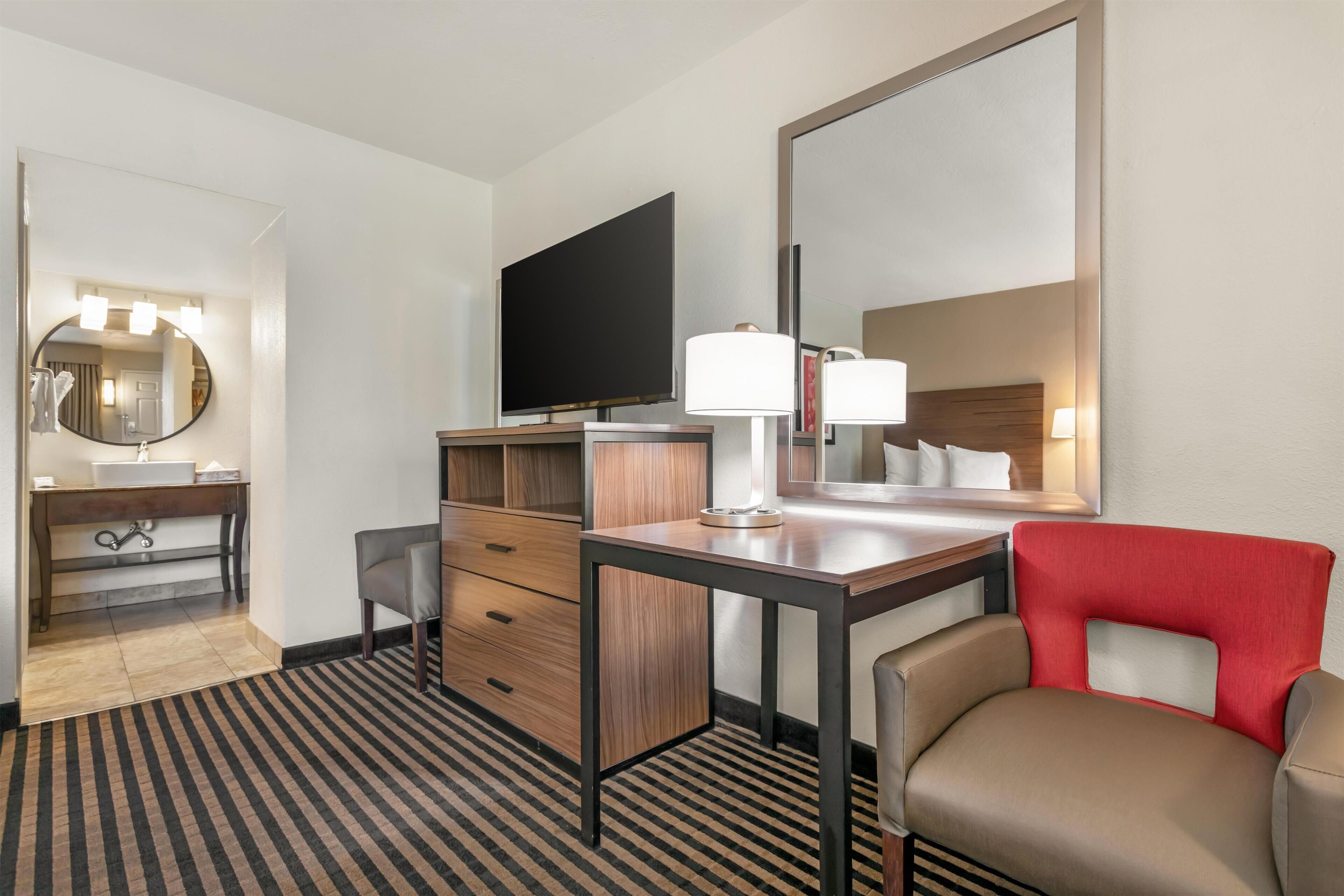A hotel room with a desk, chair, TV, and a mirror.