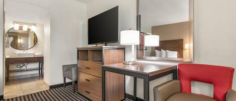 Una habitación de hotel con escritorio, silla, televisor y espejo.