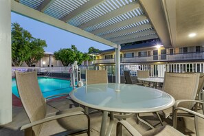 An outdoor seating area with a glass table and chairs, a pool, and a building with balconies in the background. - Best Western Town House Lodge (Modesto)