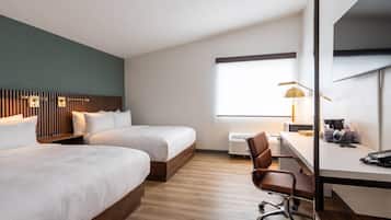 Habitación de hotel con dos camas, un escritorio, una silla, una lámpara y una ventana.