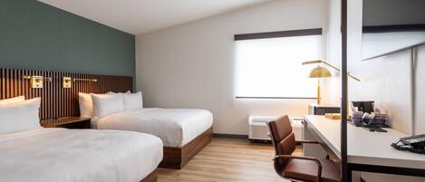 A hotel room with two beds, a desk, a chair, a lamp, and a window.