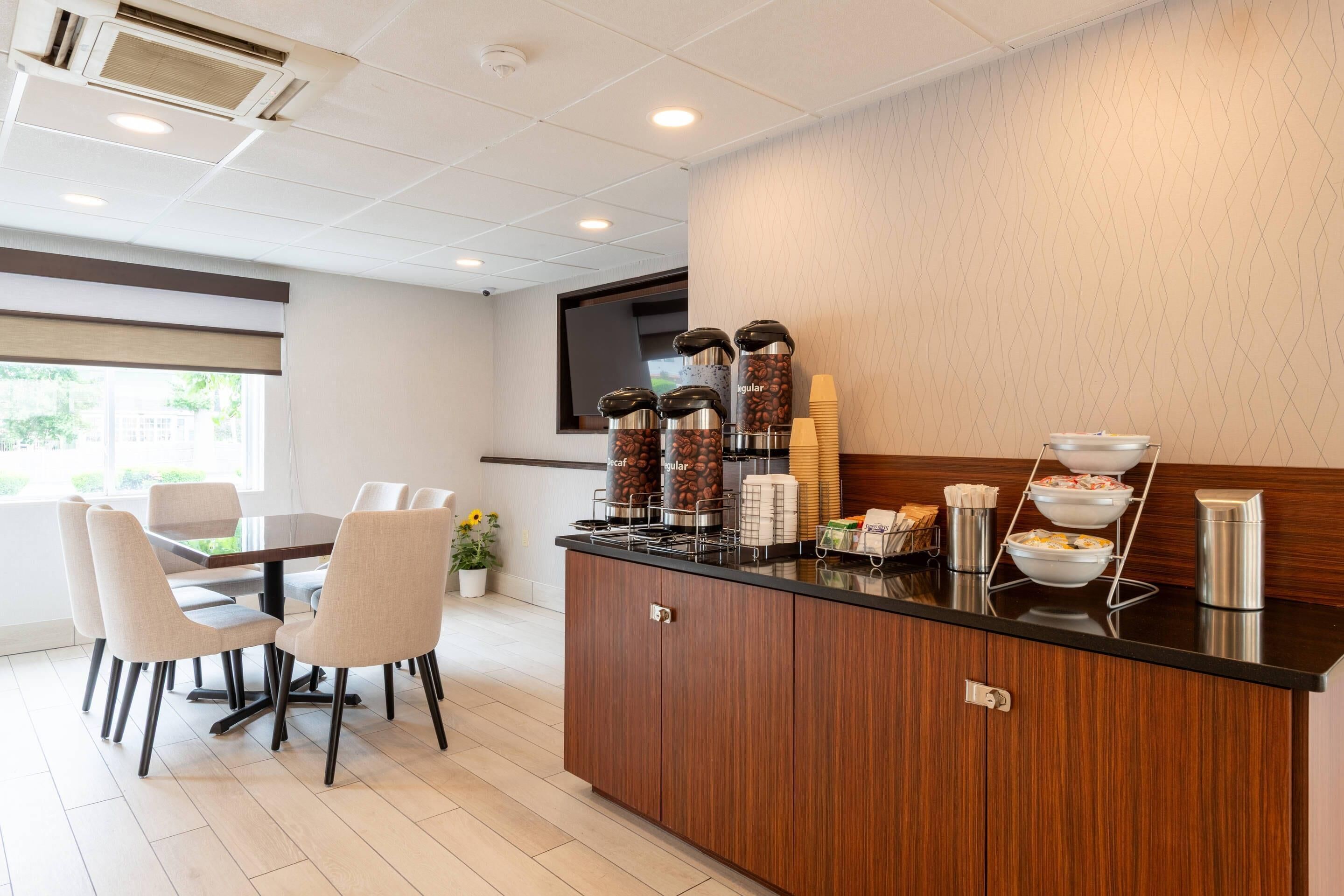 Ein Hotelzimmer mit Küchenzeile, einem Essbereich mit Stühlen, einer Kaffeestation und einem Fenster mit Blick auf Grünflächen.