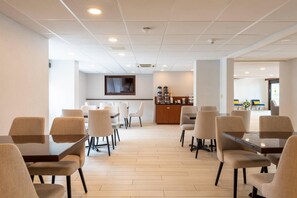 Un grand espace de restauration avec plusieurs tables et chaises, un comptoir en bois avec un coin café, et un téléviseur fixé au mur.