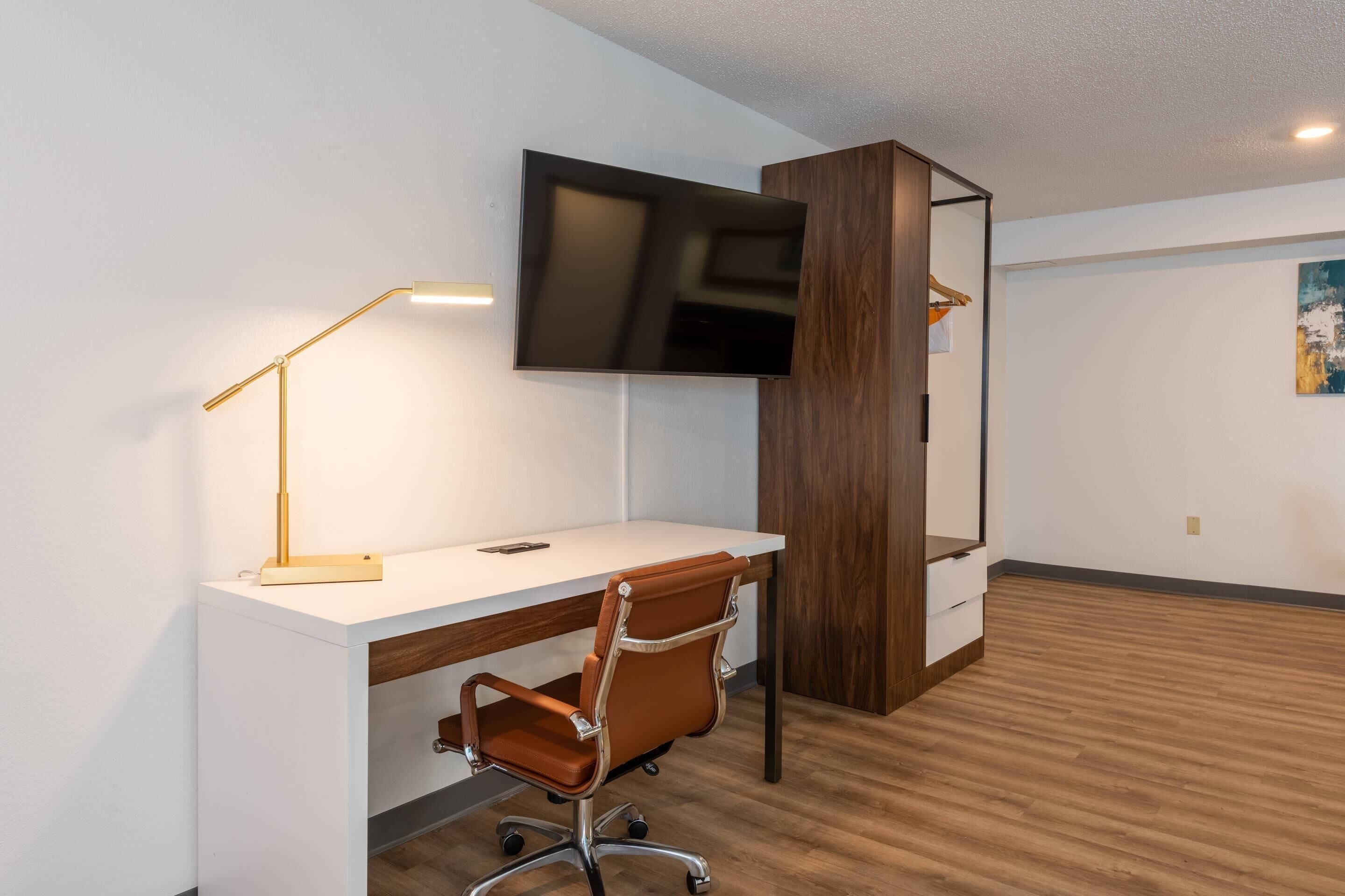 A modern office space with a desk, chair, mounted TV, and a wooden cabinet.