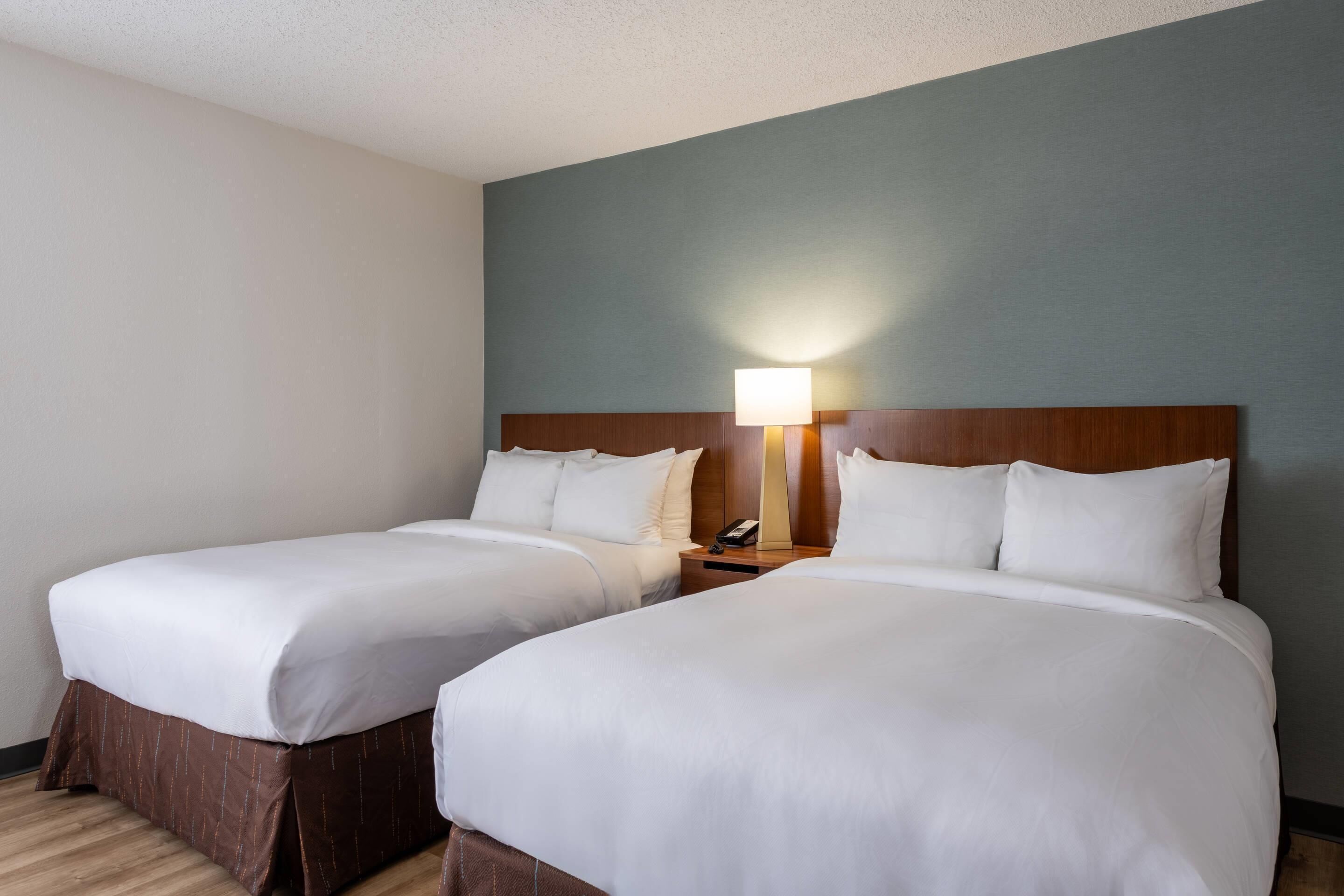 Habitación de hotel con dos camas individuales, una mesita de noche con lámpara y cabecero de madera.