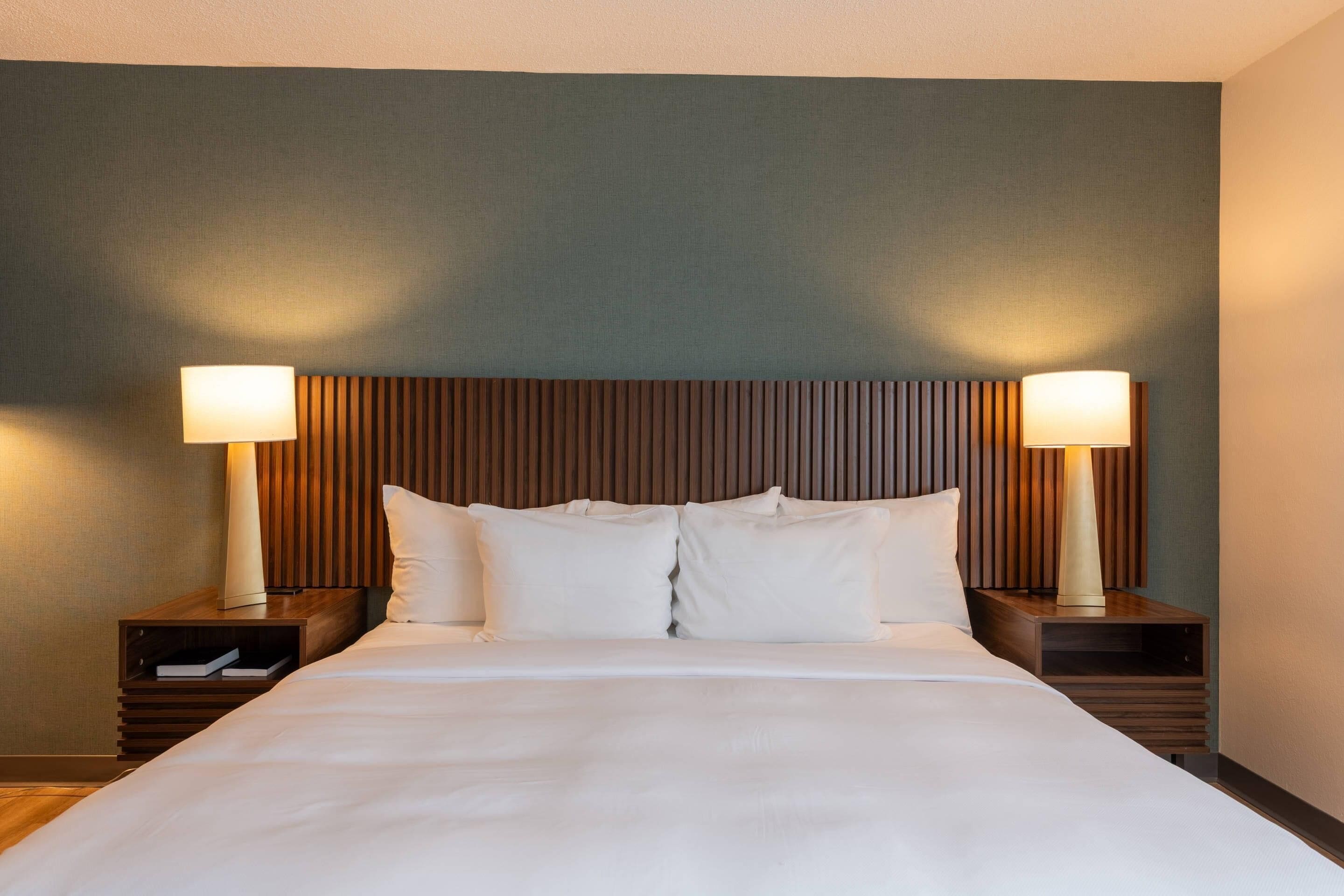 A hotel room with a large bed, two bedside tables, and a headboard with vertical slats.