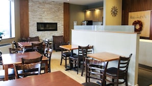 A restaurant with wooden tables and chairs, a stone wall, and a kitchen area in the background. - Welcominns Hotel Ottawa (Ottawa)