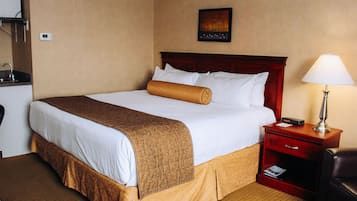A hotel room with a large bed, a bedside table with a lamp, a small desk with a telephone, and a wall-mounted thermostat.