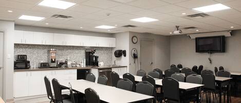 A conference room with a long table and chairs, a kitchenette with appliances, and a television on the wall.