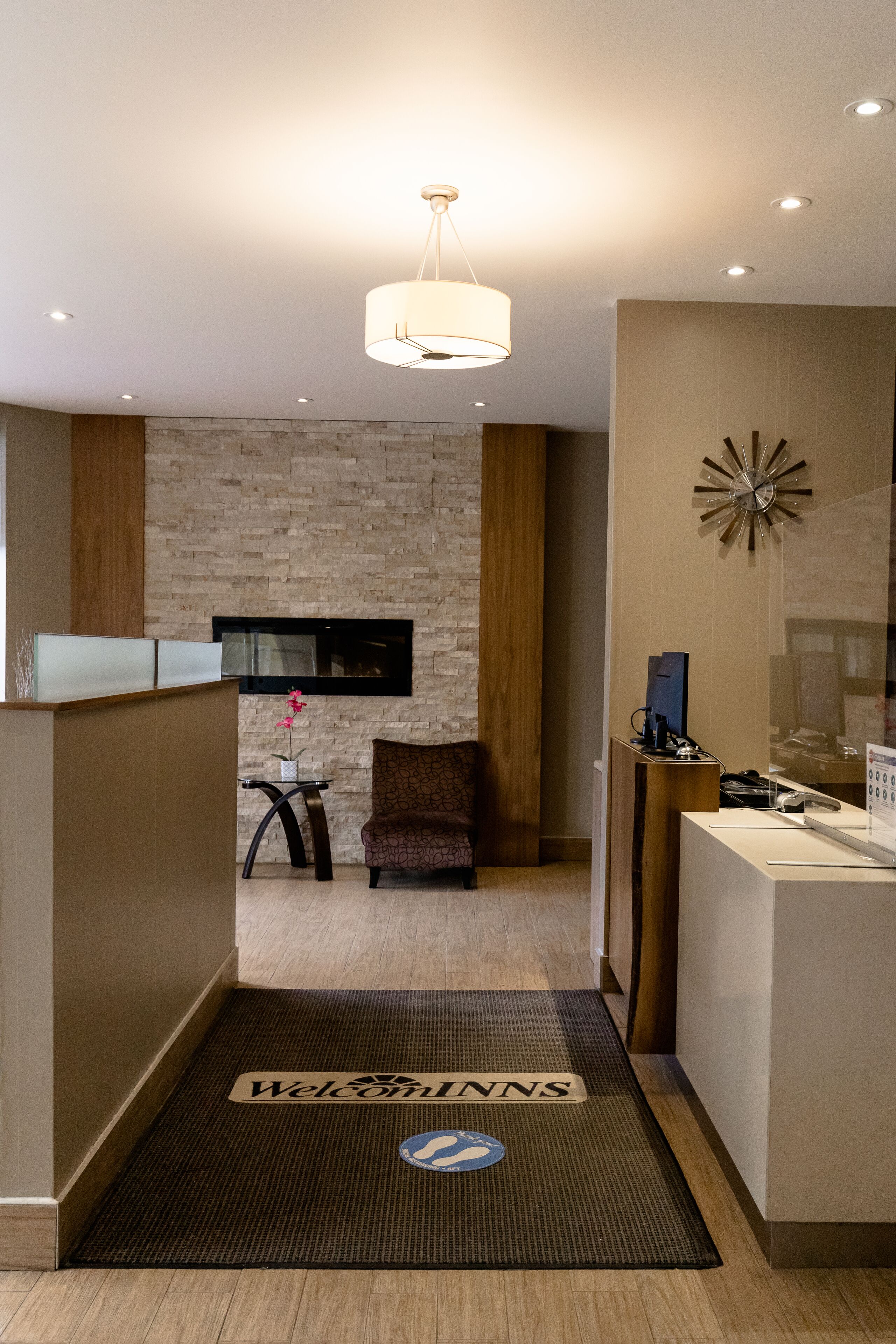 Zona de recepción de hotel con un diseño moderno, que incluye un mostrador de recepción, un área de descanso y un reloj decorativo en la pared.