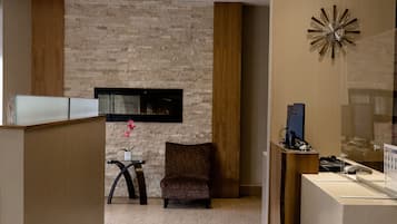 Zona de recepción de hotel con un diseño moderno, que incluye un mostrador de recepción, un área de descanso y un reloj decorativo en la pared.