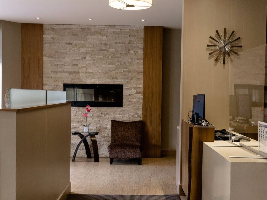 Zona de recepción de hotel con un diseño moderno, que incluye un mostrador de recepción, un área de descanso y un reloj decorativo en la pared.