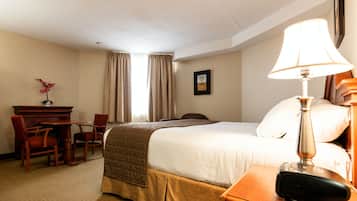 Una habitación de hotel con cama, mesita de noche, lámpara, escritorio, silla y chimenea.