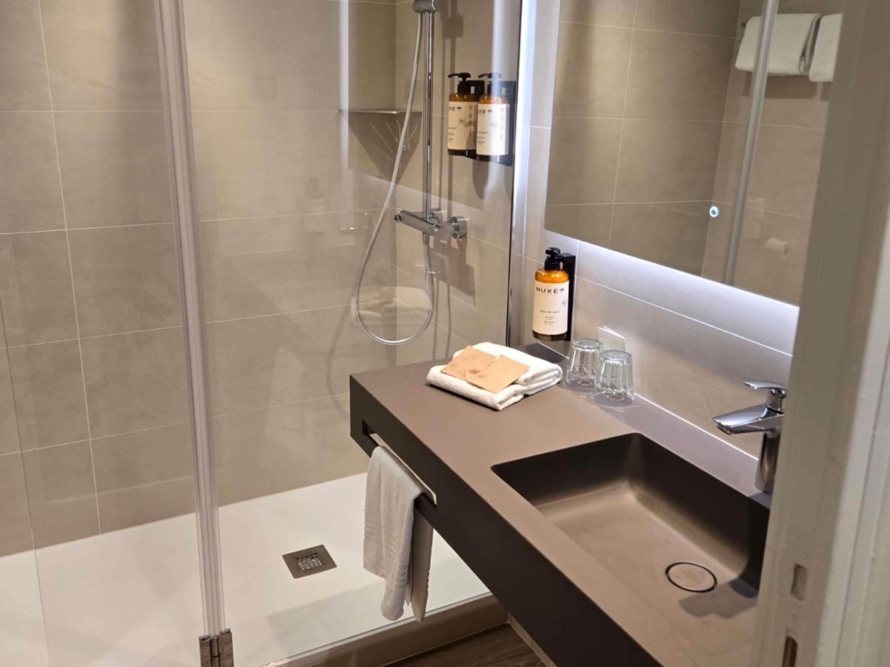 A modern bathroom with a glass-enclosed shower, a dark countertop sink, and a mirror above it.