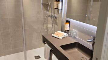 A modern bathroom with a glass-enclosed shower, a dark countertop sink, and a mirror above it.