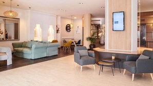 A modern living room with a sofa, armchairs, a coffee table, and a dining area. - Mercure Rennes Centre Gare (Rennes)
