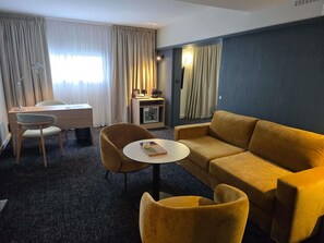 A hotel room with a sofa, two armchairs, a small round table, a desk, and a lamp. - Mercure Rennes Centre Gare (Rennes)