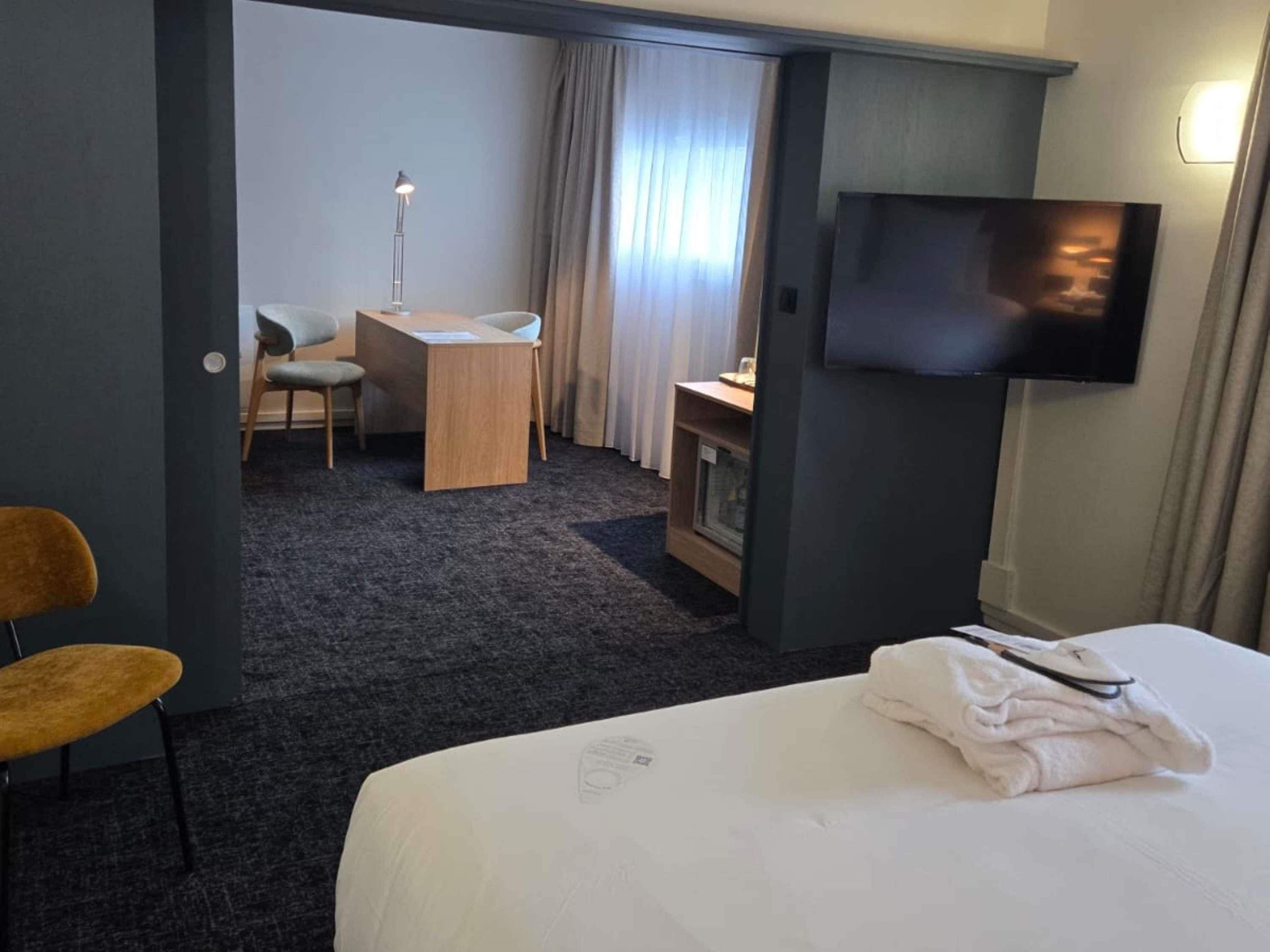 A hotel room with a bed, a desk, a chair, a television, and a window with curtains.