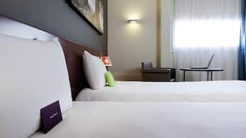 A hotel room with two beds, a desk, a chair, a lamp, and a painting on the wall.