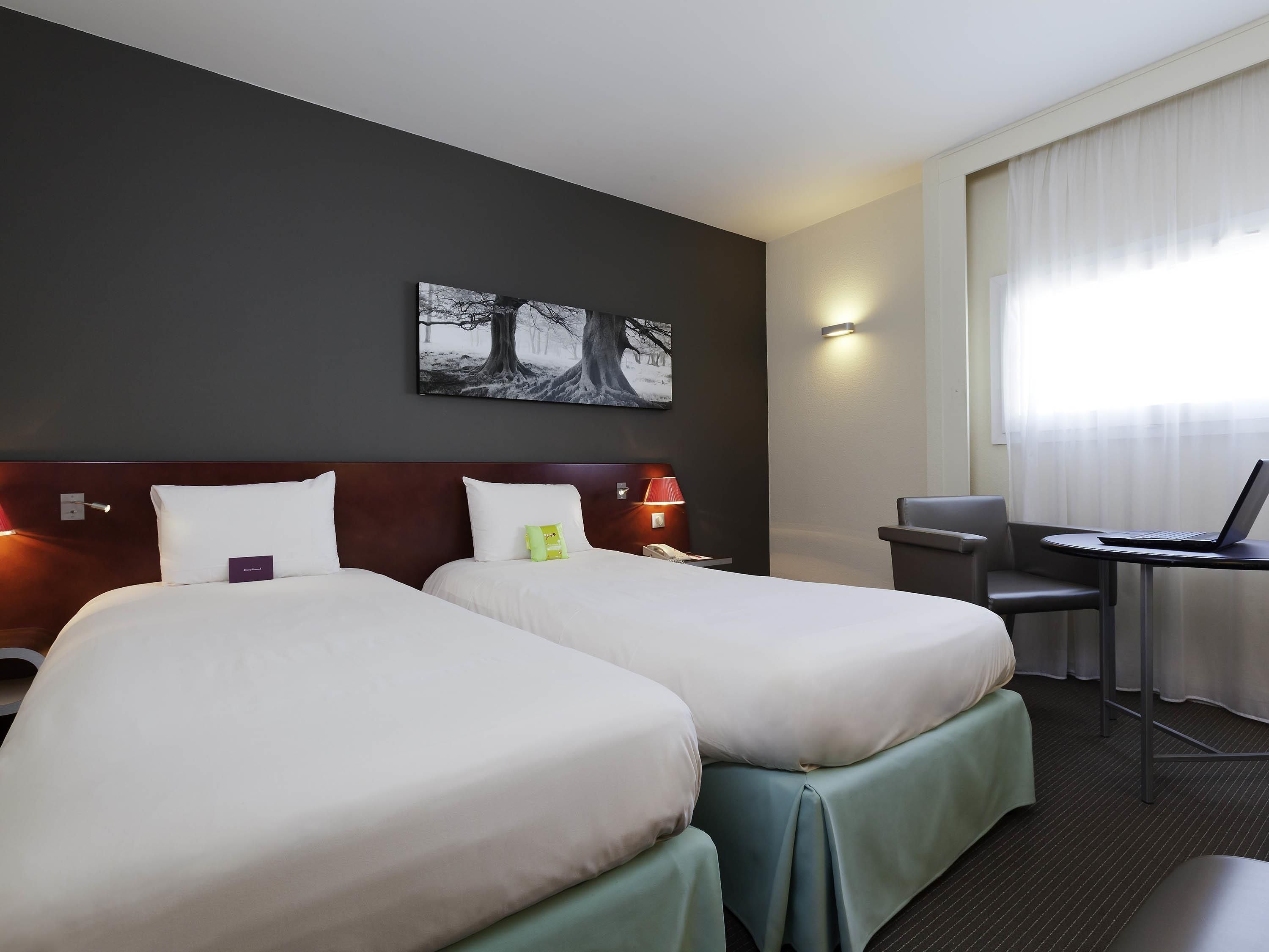 Camera d'albergo con due letti, una scrivania, una sedia e una finestra con tende.