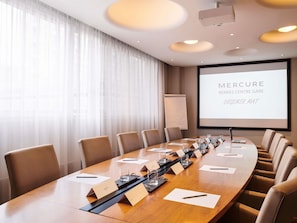 Un salón de conferencias con una larga mesa, tarjetas de identificación y una pantalla de proyector que muestra 'Mercure Rennes Centre Gare'.