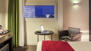A hotel room with a bed, a desk with a laptop, a chair, a small table, a window with a city view, and a curtain. - Mercure Rennes Centre Gare (Rennes)