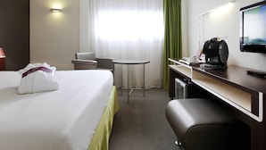 Ein Hotelzimmer mit einem Bett, einem Schreibtisch mit Kaffeemaschine, einem Sessel, einem kleinen Tisch und einem Fernseher.