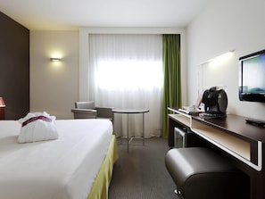 A hotel room with a bed, a desk with a coffee maker, a chair, a small table, and a television. - Mercure Rennes Centre Gare (Rennes)