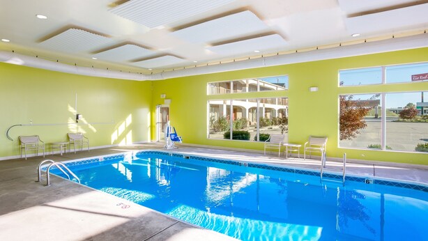 En indendørs swimmingpool med klart vand, en dybdemarkering på 6 meter, og udsigt til det fri gennem store vinduer.