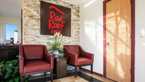 A hotel lobby with two red leather chairs, a coffee machine, and a wall-mounted sign reading 'Red Roof Inn'. - Red Roof Inn Vincennes (Vincennes)