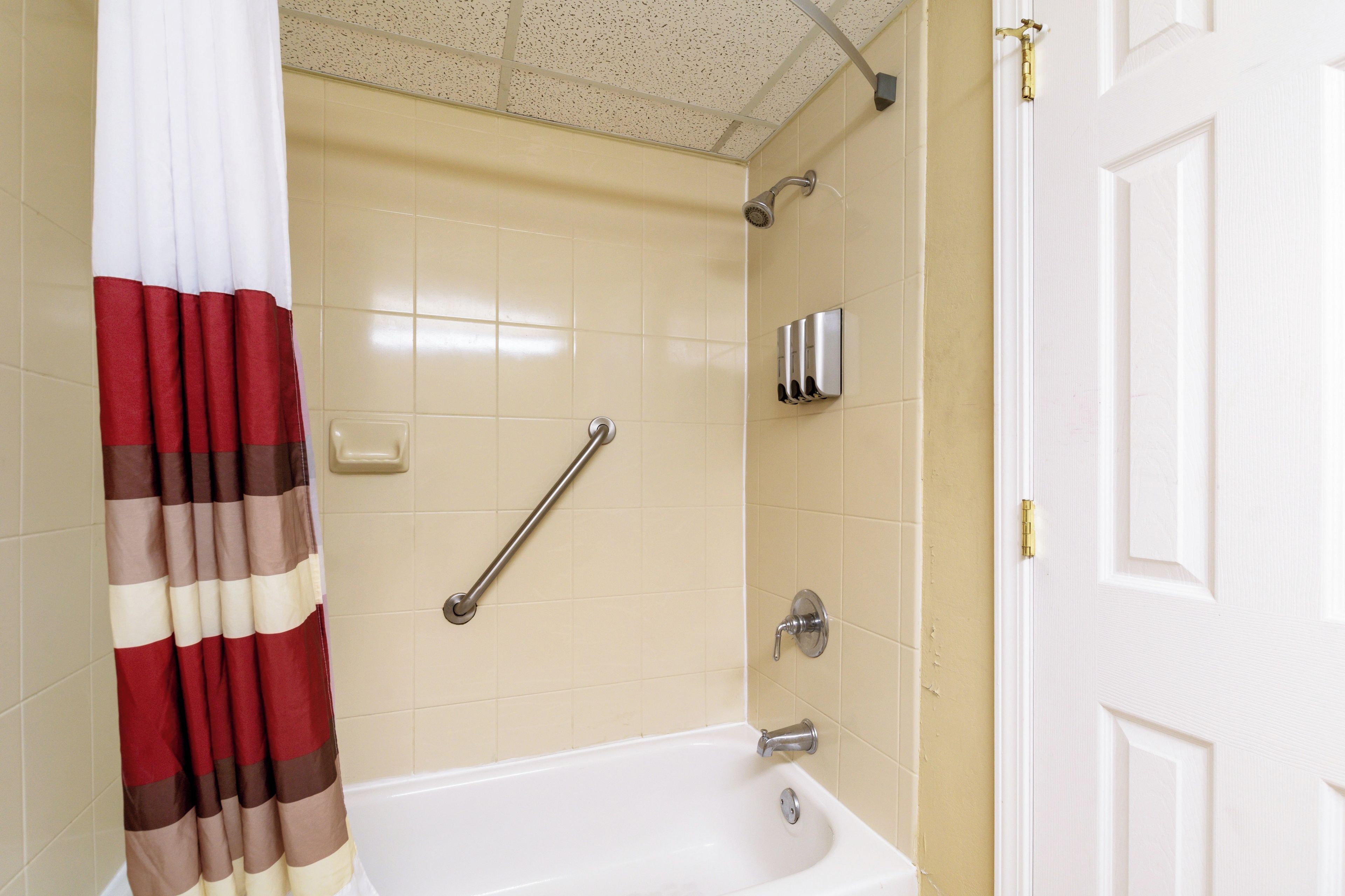 A bathroom with a white bathtub, a shower with a handheld showerhead, a handrail, and a towel rack.