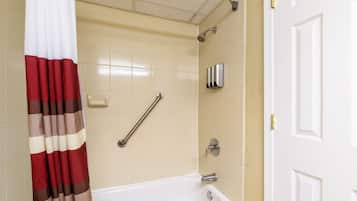 A bathroom with a white bathtub, a shower with a handheld showerhead, a handrail, and a towel rack.