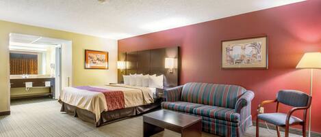 A hotel room with a bed, a sofa, a chair, a small table, and a painting on the wall.