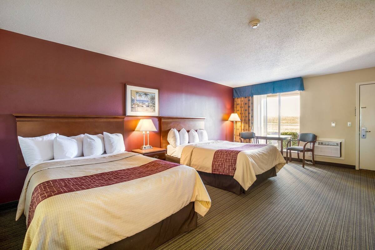 A hotel room with two beds, a desk, a chair, a window with a view, and a ceiling light.