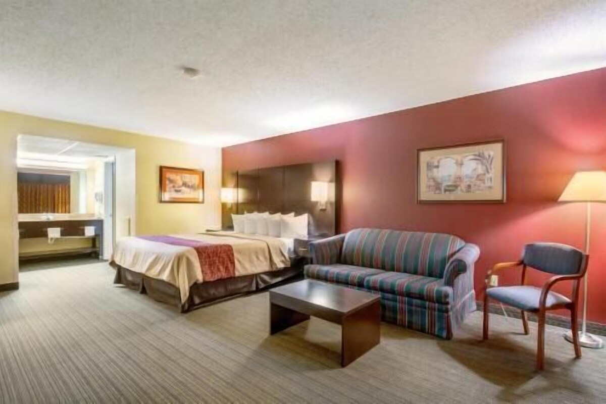 A hotel room with a bed, a sofa, a chair, a coffee table, and a painting on the wall.