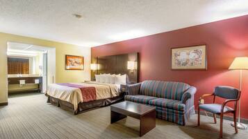 A hotel room with a bed, a sofa, a chair, a small table, and a painting on the wall.
