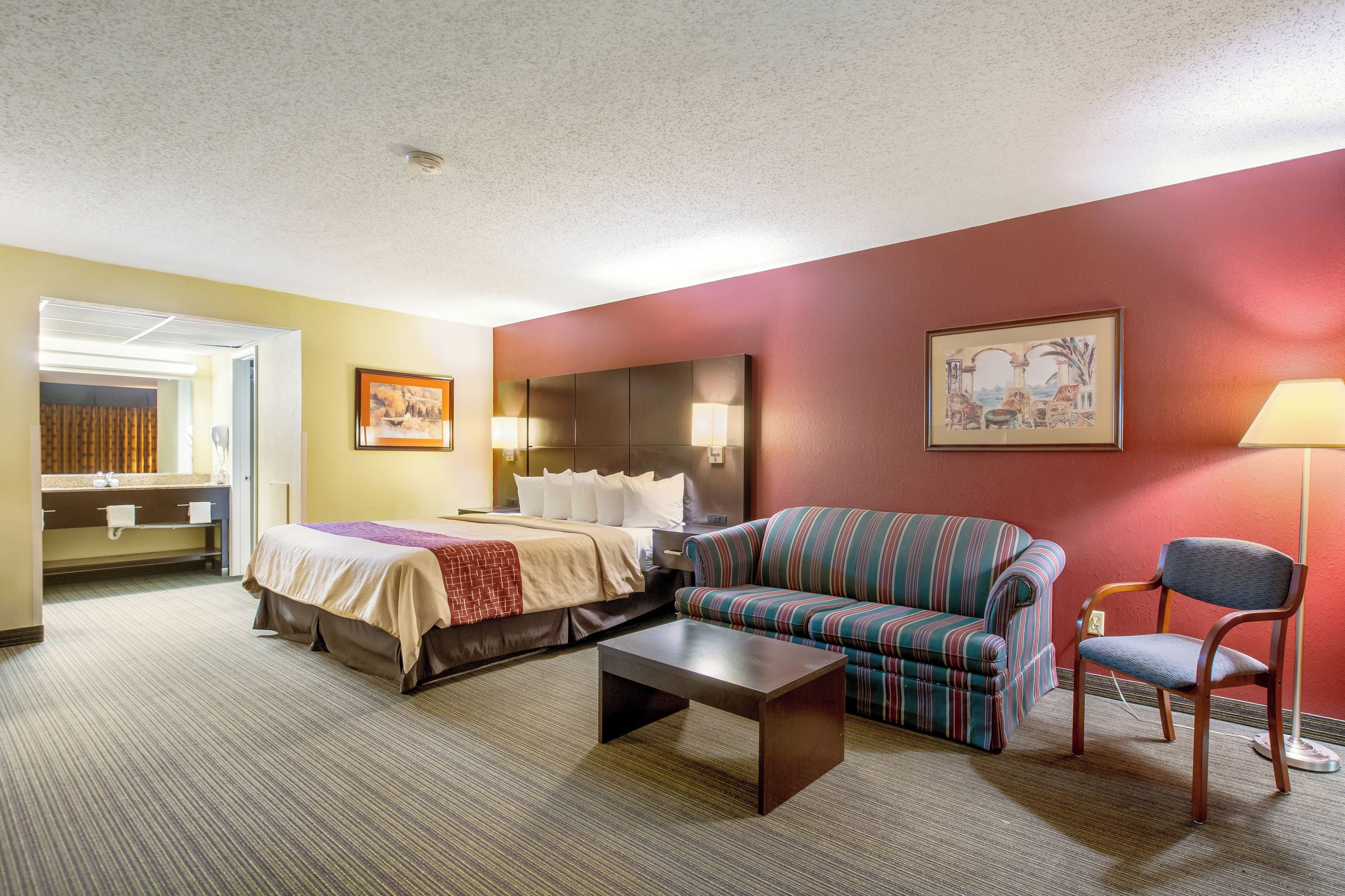 Habitación de hotel con cama, sofá, sillón y una mesita.