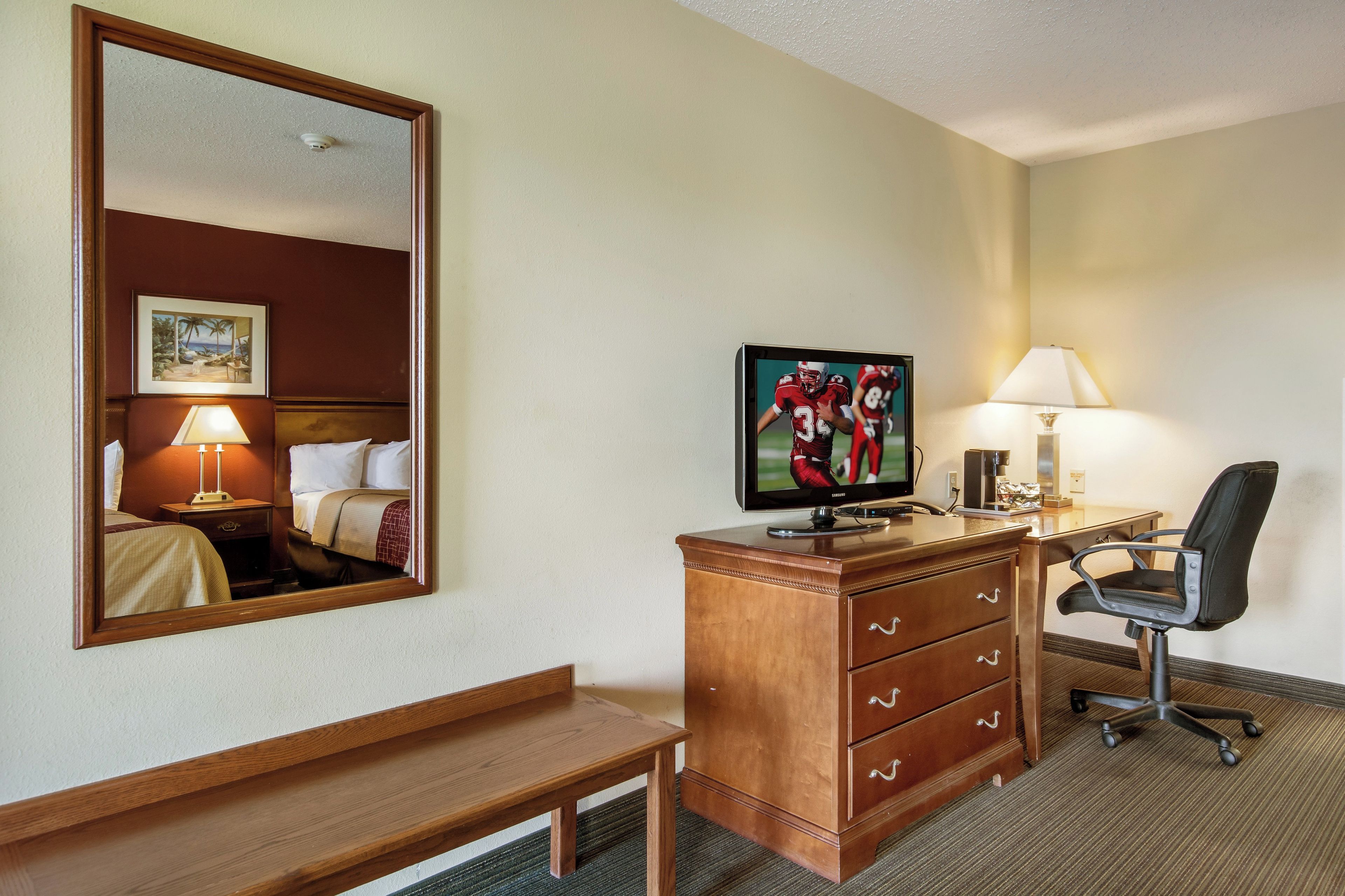 Une chambre d’hôtel comprenant un lit, un bureau avec un ordinateur, une chaise, une télévision et un miroir.