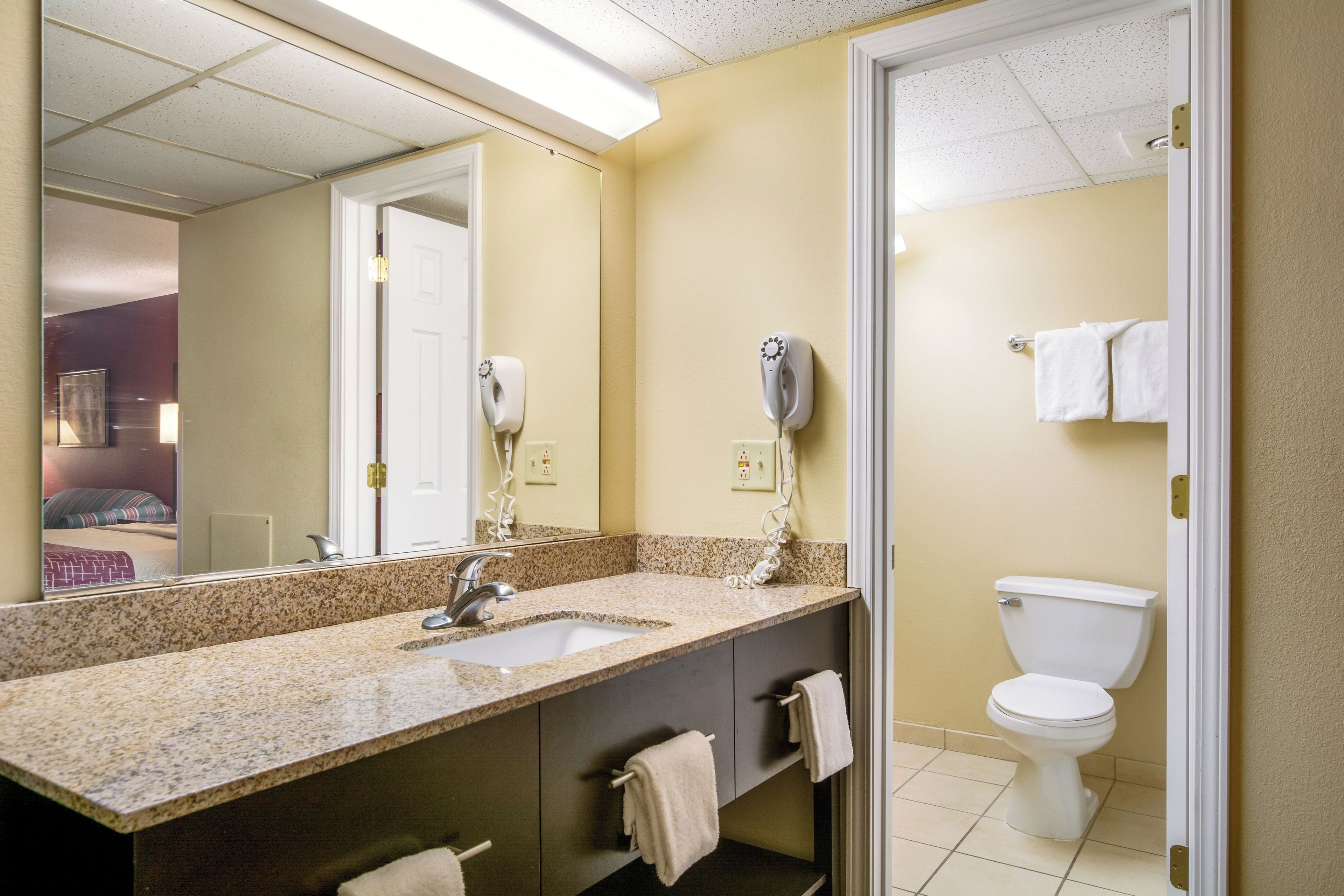 A bathroom with a granite countertop, a sink, a mirror, a towel rack, a toilet, and a hairdryer.