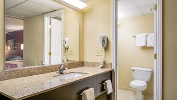 A bathroom with a granite countertop, a sink, a mirror, a towel rack, a toilet, and a hairdryer.