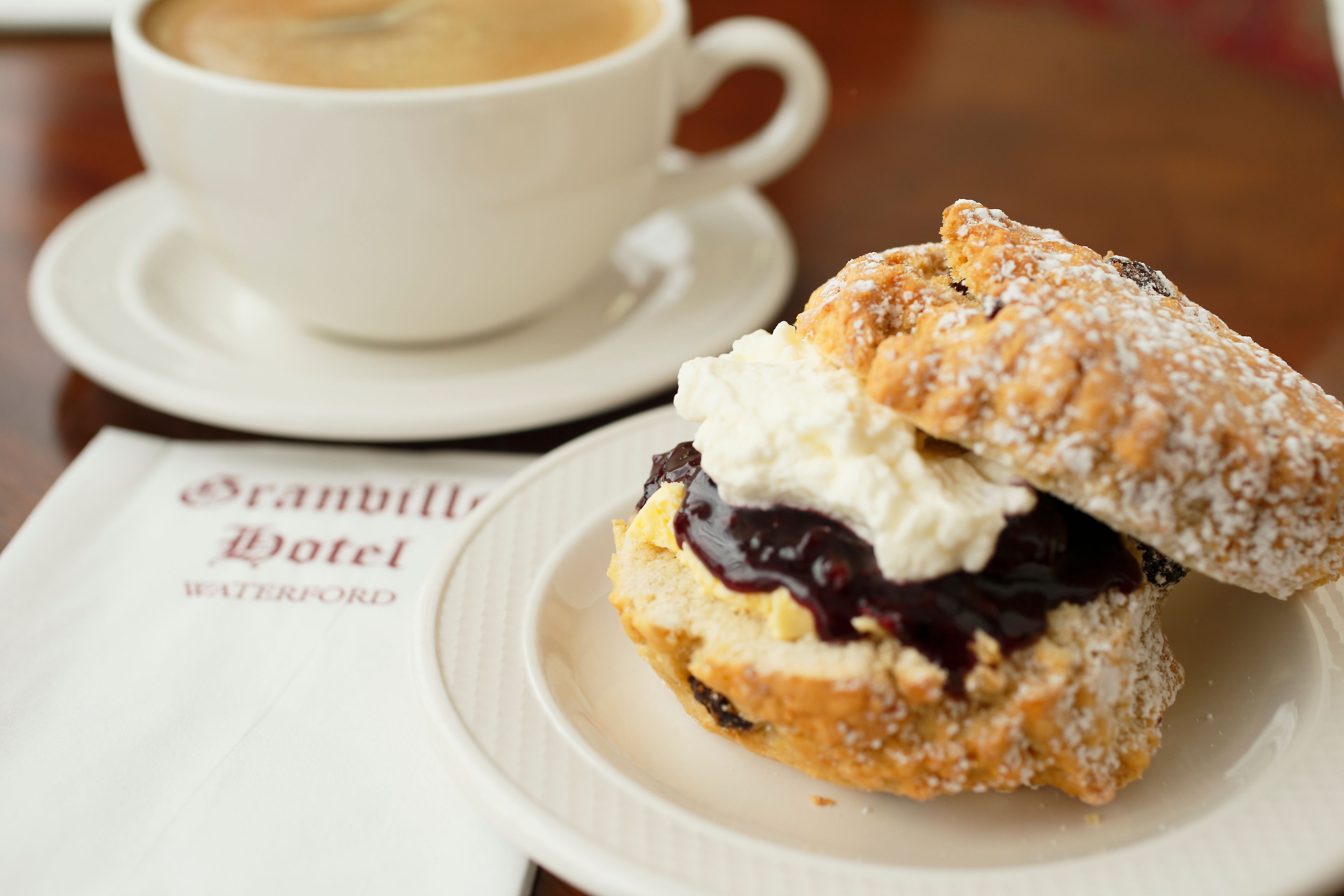 Sobremesa com chantilly e compota de frutos vermelhos num prato, acompanhada por uma chávena de café num pires.