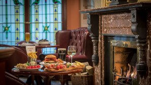 A dining table with a variety of food and drinks, a fireplace, and stained glass windows in the background.