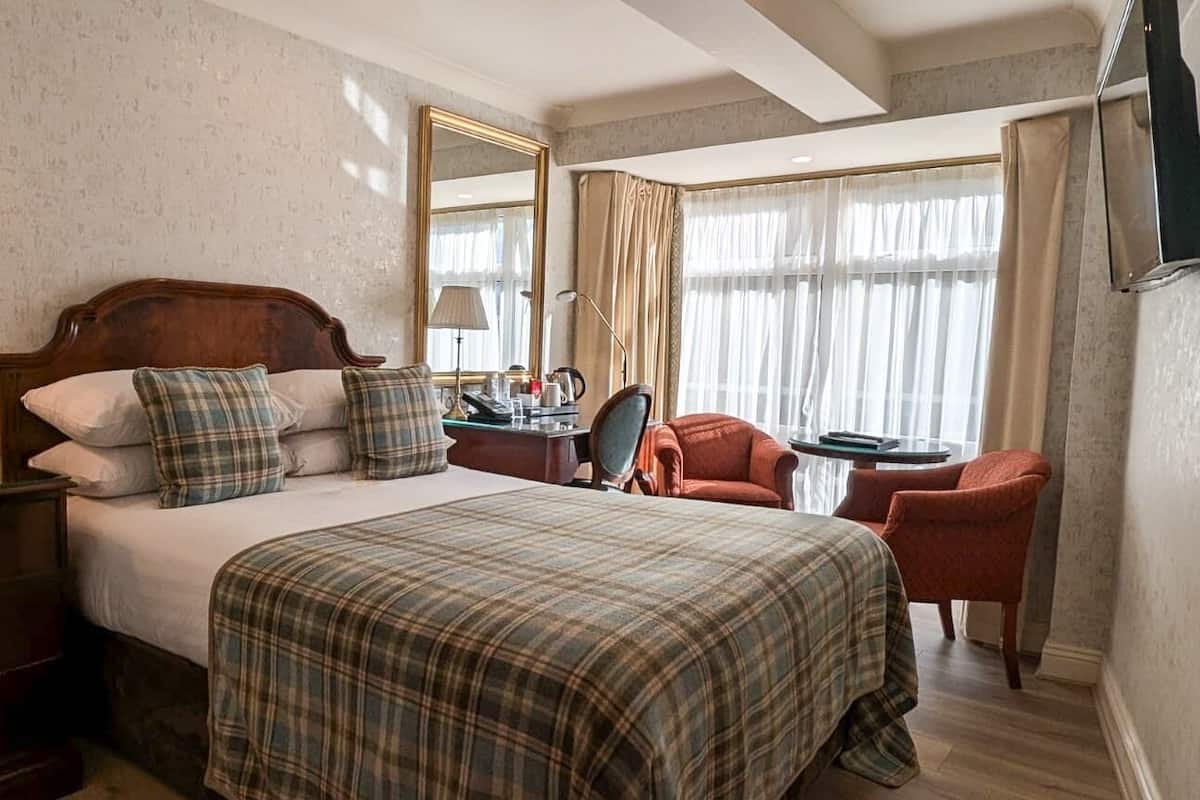 Une chambre d’hôtel avec un grand lit, une commode en bois, un bureau avec une chaise, une table ronde et un grand miroir.