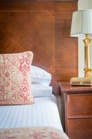 Una cama bien hecha con un cojín estampado, una lámpara de noche y una mesita de madera.