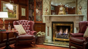 A traditional room with a fireplace, leather armchairs, a table with a lamp, and a large mirror above the mantelpiece.