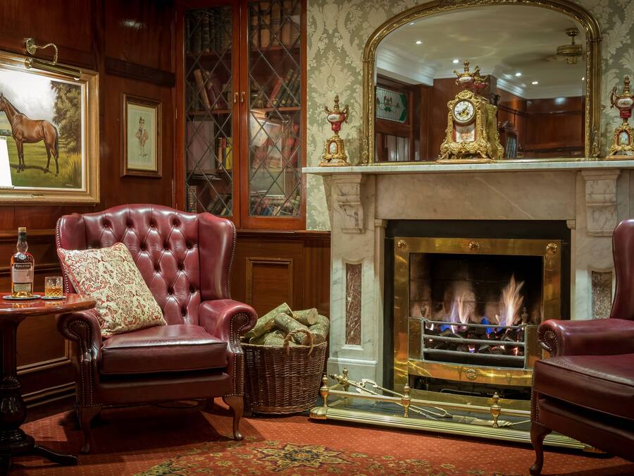 A traditional room with a fireplace, leather armchairs, a table with a lamp, and a large mirror above the mantelpiece.