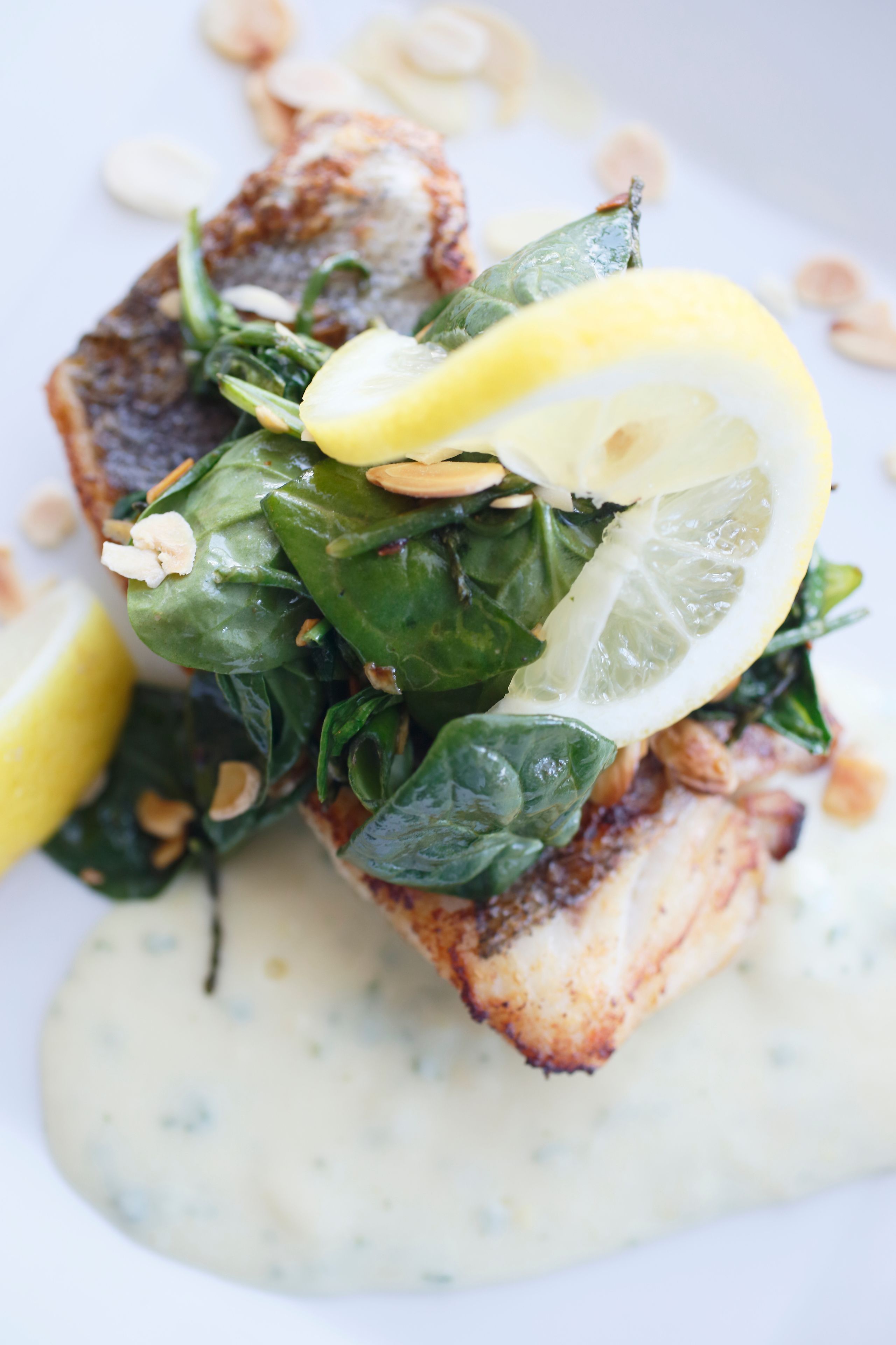 A dish with fish, spinach, lemon, and a creamy sauce.