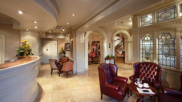 A spacious lobby with a curved reception desk, leather armchairs, and a staircase leading to upper floors.